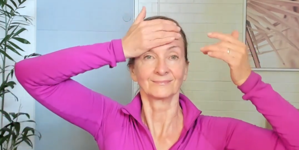 a old lady in pink jacket performing forehead smoother exercise